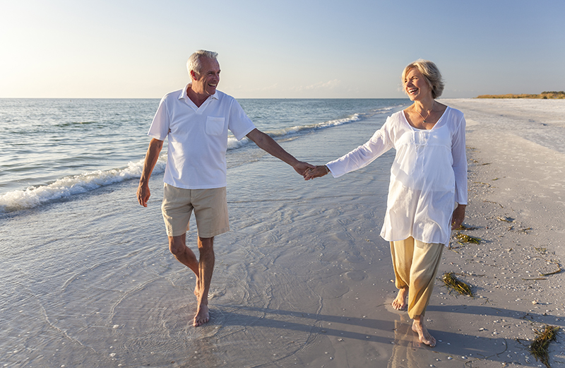 elderly couple holding hands on the beach